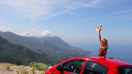 a woman waving her hat out of the car with a view of the mountain bay
