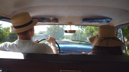 Young couple in hats driving on country road in classic vintage car. Unrecognizable pair riding into old auto. Man and woman sitting at the front seat of a retro automobile. Trip concept. Slow motion