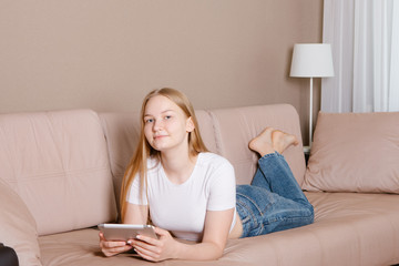 Young casual woman relaxing on couch at home using tablet in daylight.