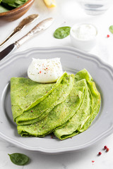 Green thin pancakes with spinach, poached egg, sour cream, lemon and aromatic herbs, delicious healthy food