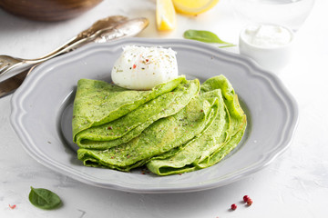 Green thin pancakes with spinach, poached egg, sour cream, lemon and aromatic herbs, delicious healthy food