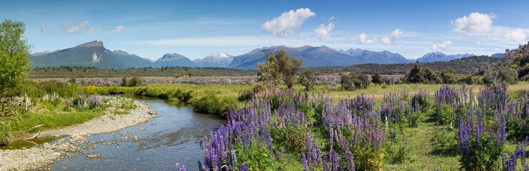 Obraz premium Panoramic view of a small river and mountain range approaching the fiordland area of New Zealand. Focus is on the stream and mountains.