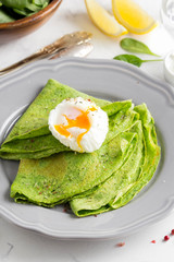 Green thin pancakes with spinach, poached egg, sour cream, lemon and aromatic herbs, delicious healthy food