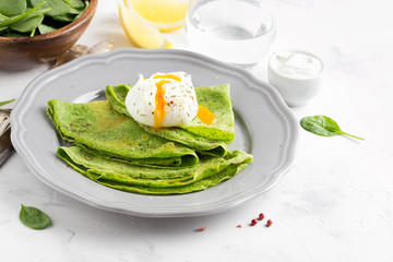 Green thin pancakes with spinach, poached egg, sour cream, lemon and aromatic herbs, delicious healthy food