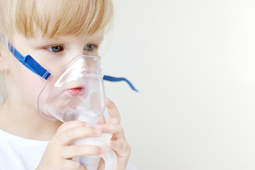 Little girl in a mask for inhalations, making inhalation with nebulizer at home inhaler on the...