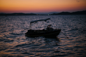 Beautiful view of empty sailing boat moored at the sea shore on orange and pink sunset. Dusk. Greece