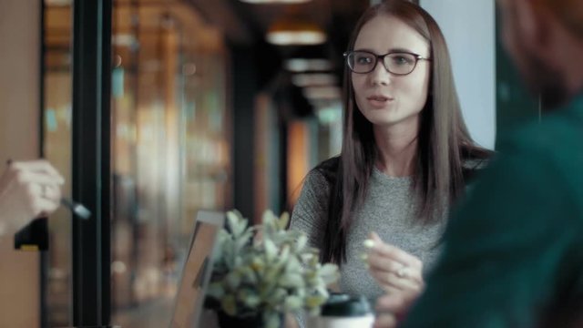 Attractive european female team leader in glasses smiles and actively gesticulates explains the task creative business team meeting in modern start up office people group teamwork discussing project