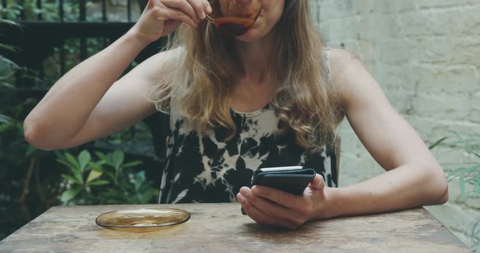 Young woman drinking coffee and using smartphone in yard