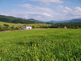 a large white house on a green lawn in the Carpathian village on the background of shallow mountains