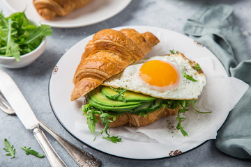 croissant sandwich with avocado, arugula and fried egg for breakfast