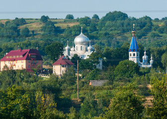 The tops of church temples with colorful roofs and domes against the background of green mountain slopes