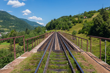 Fototapeta na wymiar Old iron bridge with rails against the background of green trees and huge mountains