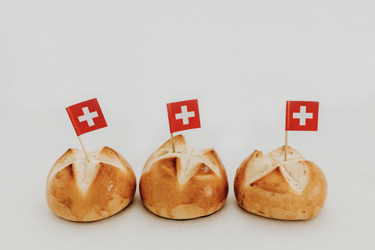 Swiss bread buns called in German 1. Augustweggen baked in Switzerland to celebrate Swiss National Day on August 1st. Swiss flag with white cross on red background.  White background, isolated.