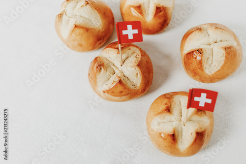 Swiss bread buns called in German 1. Augustweggen baked in Switzerland to celebrate Swiss National Day on August 1st. Swiss flag with white cross on red background.  White background, isolated.
