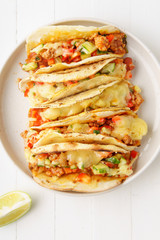 Mexican tacos with chili con carne and grated cheese served on a plate over white wooden table