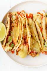 Mexican tacos with chili con carne and grated cheese served on a plate over white wooden table
