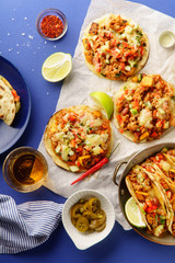 Overhead image of mexican tacos with chili con carne, sweet potatoes and grated cheese served over a blue background