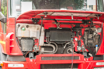 Fixing and repairing big heavy red semi truck with open hood on the street as regular maintenance service, close up