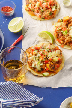 Overhead image of mexican tacos with chili con carne, sweet potatoes and grated cheese served over a blue background