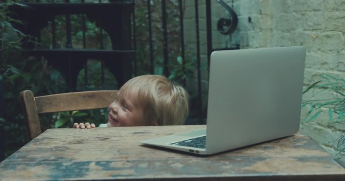 Little toddler watching video on laptop outdoors