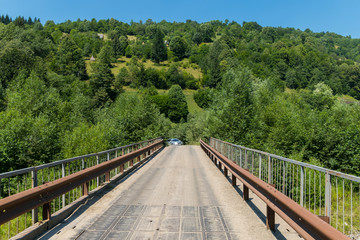 Fototapeta premium Old car bridge with rusty railing against the background of a green slope with trees