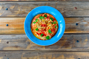 Chickpea hummus and tahini topped with pine nuts,olive oil, pepper, parsley, spices on a rustic wooden table. Hummus Traditional Middle Eastern food commonly served in a pita.