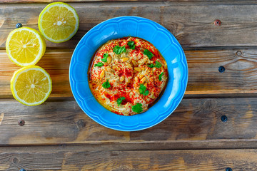 Chickpea hummus and tahini topped with pine nuts,olive oil, pepper, parsley, spices on a rustic wooden table. Hummus Traditional Middle Eastern food commonly served in a pita.