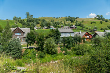 A village with two-storey cottages and small houses on the background of a green mountain and a blue sky