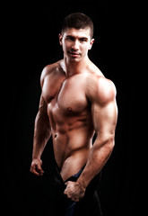 Fototapeta premium kulturysta pozowanie. Piękny sportowy facet męski moc. Fitness umięśniony mężczyzna na czarnym tle.