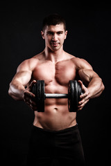 Fototapeta na wymiar Muscular bodybuilder guy doing exercises with dumbbell over black background