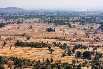 Top view or aerial shot from top of a rocky mountain of fresh green and yellow rice fields in sunny day of summer season in rural village of india.