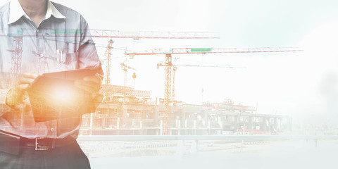 Engineer standing using tablet control and manage work at construction site.