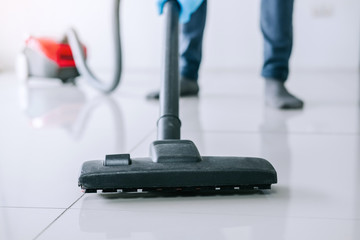 Housekeeping and housework cleaning concept, Happy young man in blue rubber gloves using a vacuum cleaner on floor at home