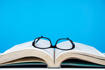 Education concept. An old book, eyeglasses over blue background