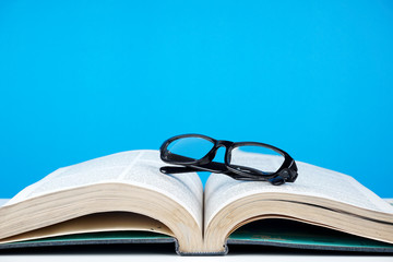 Education concept. An old book, eyeglasses over blue background