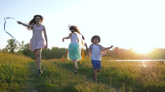 family leisure in nature, happy active children with ribbons and toy mills running on green grass in bright sunlight