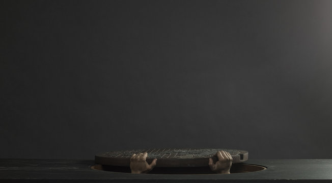 Hands lifting manhole cover from underneath