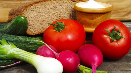 Fresh vegetables and rye bread on wooden background.