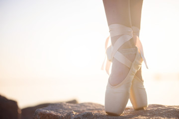 Talented ballerina with pointe shoes on the beach at sunset