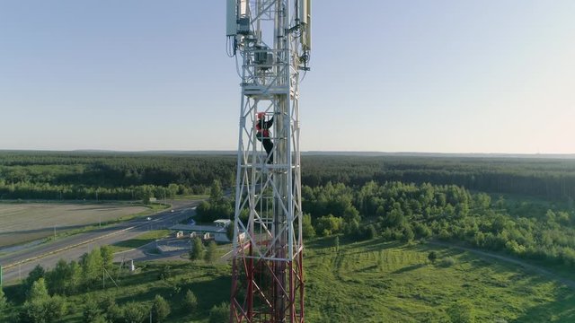 Aerial Footage servicing cellular antenna, worker dressed in uniform and helmet climbs the stair on telecommunication tower