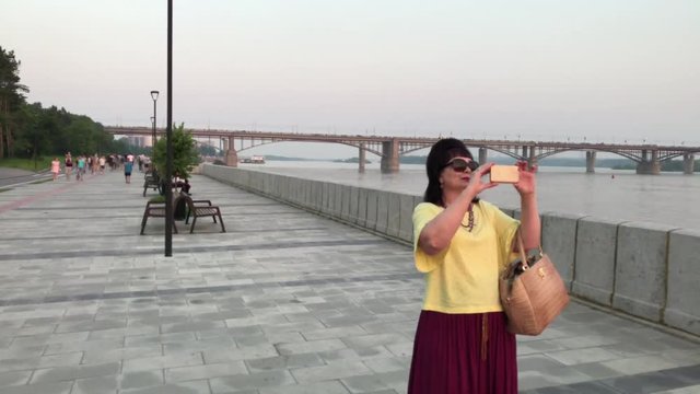 woman shoots video on a smartphone, on the embankment of the river of the city of Novosibirsk at sunset of the day