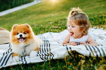 Little girl and pets. The girl and a dog lying on a blanket on a green park. Sunset time. Pedigree dogs Spitz. Funny animals. Outdoor picnic.
