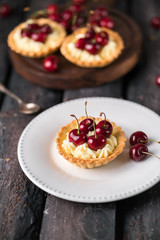 homemade cherry tart with custard and cherries on white plate, on old wooden backdrop, brown colour