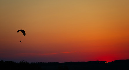 Man flight on a paraglider in a cloudless sky at sunset.