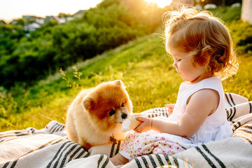 a little girl sitting on a blanket and feeding the dog ice cream. Sunset in the background