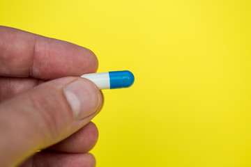 Hand holding drugs pills capsule on yellow background