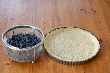 empty tarte ground with a sieve full of blueberries on a wooden table