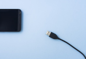 Mobile phone with USB plug isolated on blue pastel background, space for text. Flat lay.