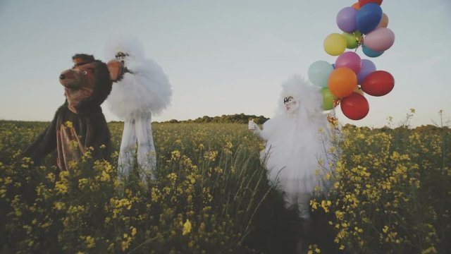 Two funny clowns mime in white air suits and with colored balloons walk around the field and have fun with a cheerful bear.