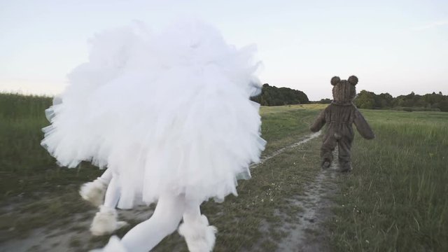 Two funny clowns mime in white air suits are chasing a ridiculous bear along a country road in the field.